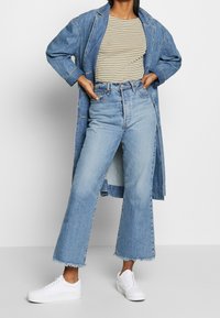 Denimjacka, randig topp, högmidjade ljusblå jeans med fransar, och vita sneakers. Avslappnad outfit med lager på lager-texturer.