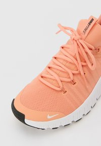 Nike Flex tenisice u svijetlo breskvastoj tkanini, s prozračnom teksturom, ravnim vezicama i bijelom srednjom potplatom s crnim detaljima.