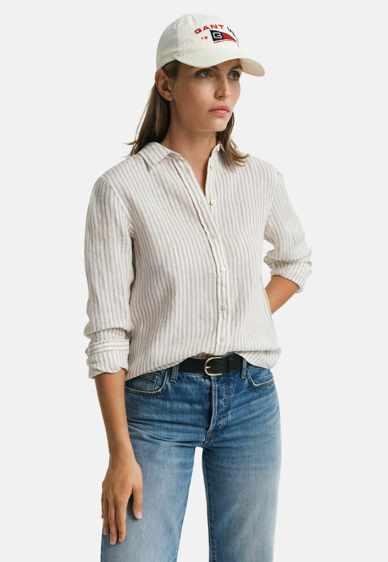Licht beige gestreepte button-up shirt met kraag, gecombineerd met blauwe denim jeans en een witte pet met rode letters en een logo.