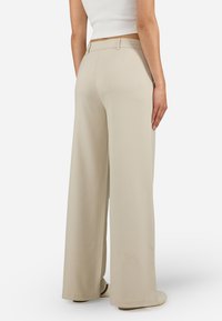 Beige wide-leg trousers with a smooth texture, high waistband, and subtle pleats. The fabric drapes elegantly over the legs.
