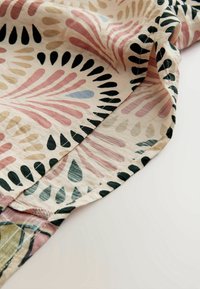 Tissu doux avec ourlet courbé et motifs abstraits multicolores de feuilles en rose, noir, beige et bleu sur un fond clair.