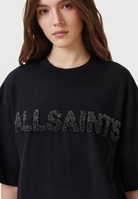 Camiseta negra de manga corta con la inscripción "ALLSAINTS" en detalles de cuentas negras texturizadas, cuello redondo y un corte relajado.