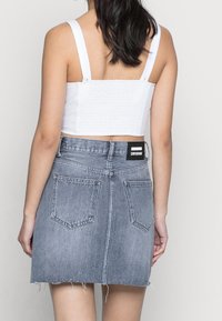 Woman wearing a white cropped tank top and a high-waisted, faded blue denim skirt with back pockets and a brand label.