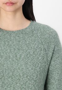 Světle zelený svetr vyrobený z texturovaného pleteného materiálu. Disponuje klasickým žebrovaným kulatým výstřihem a raglánovými rukávy.