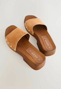 Sandales à glissière en suede tan avec une plateforme en bois et de grands clous en or le long de la sangle. Comprend un logo sur la semelle intérieure.