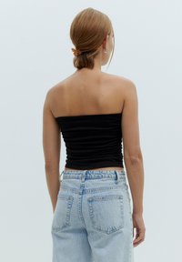 Zwarte strapless top met geplooide textuur, gecombineerd met lichtblauwe high-waisted jeans met achterzakken. Minimalistisch ontwerp en geen patronen.