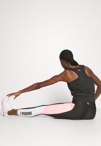 Czarny sportowy tank top, dopasowane czarne i różowe legginsy z białym akcentem oraz białe buty sportowe. Osoba rozciąga się na boki.
