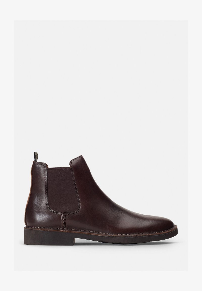 Botte Chelsea en cuir marron avec panneaux latéraux élastiques et une languette. La pointe ronde et les coutures sur la semelle ajoutent de la texture et du design.