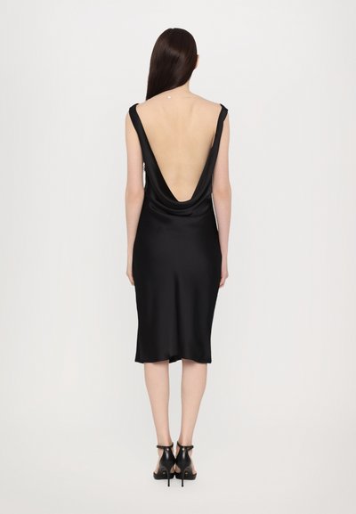 Vestido de satén negro con un profundo escote en V en la parte posterior y forma ajustada, con un dobladillo a la altura de la rodilla, complementado con sandalias de tacón alto negras con tiras.
