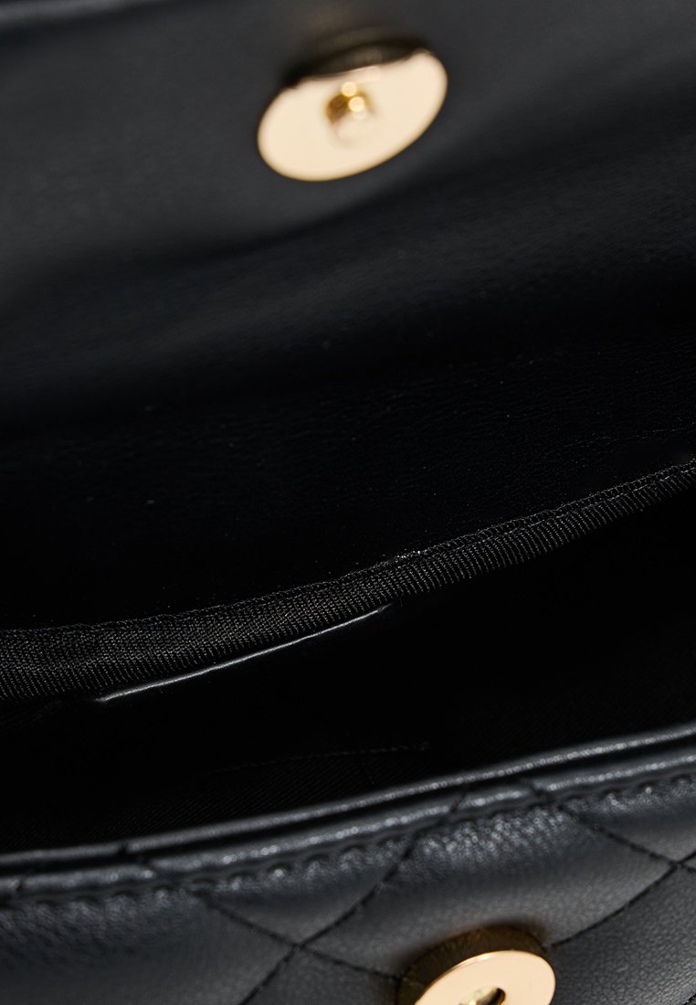 Interno della borsa nera in pelle trapuntata con chiusura a bottone a scatto dorato, caratterizzato da una texture liscia e una fodera in tessuto nero.