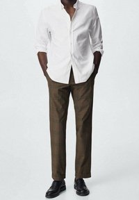 Biała koszula z guzikami, brązowe spodnie w kratę, dopasowany krój i czarne buty. Koszula ma klasyczny kołnierzyk; spodnie mają wzór w kratkę.