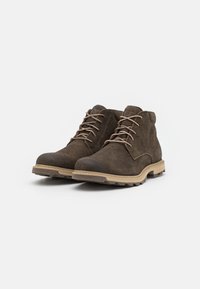 Botas de tobillo de ante marrón con suelas de goma beige, punta redonda y cordones marrones. Diseñadas con un acabado texturizado y suela resistente para mayor tracción.