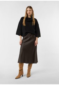 Czarny, oversize'owy sweter z grubym kołnierzem, w połączeniu z błyszczącą, brązową satynową spódnicą midi oraz beżowymi, wysokimi kozakami za kolano o spiczastych noskach.