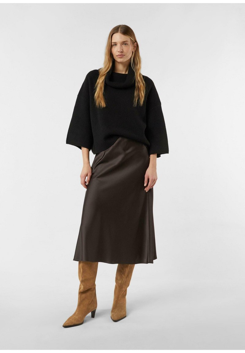 Czarny, oversize'owy sweter z grubym kołnierzem, w połączeniu z błyszczącą, brązową satynową spódnicą midi oraz beżowymi, wysokimi kozakami za kolano o spiczastych noskach.