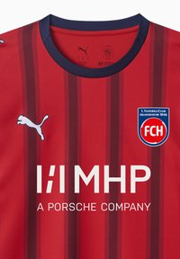 Röd fotbollströja med vertikala vinröda ränder, rund marinblå krage, vit Puma-logotyp, lagmärke och sponsortext i fetstil vita bokstäver.