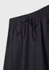 Czarne spodnie z elastycznym pasem, z zawiązywanym sznurkiem z przodu, pokazujące teksturę materiału i zgromadzone detale pasa.