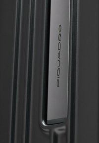 Valigia rigida nera con manico argento su cui è inciso il nome del marchio "Piquadro", che evidenzia un design elegante e moderno.