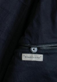 Námornícka látka s hladkou textúrou, obsahujúca čierny zips, strieborný gombík a štítok s nápisom "Pokým nás smrť nerozdelí" v bielom písme.