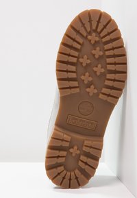 Hnědá gumová podrážka s hlubokým vzorem, na které je logo Timberland. Horní část má hladkou, jemnou texturu, která ladí s designem podrážky.
