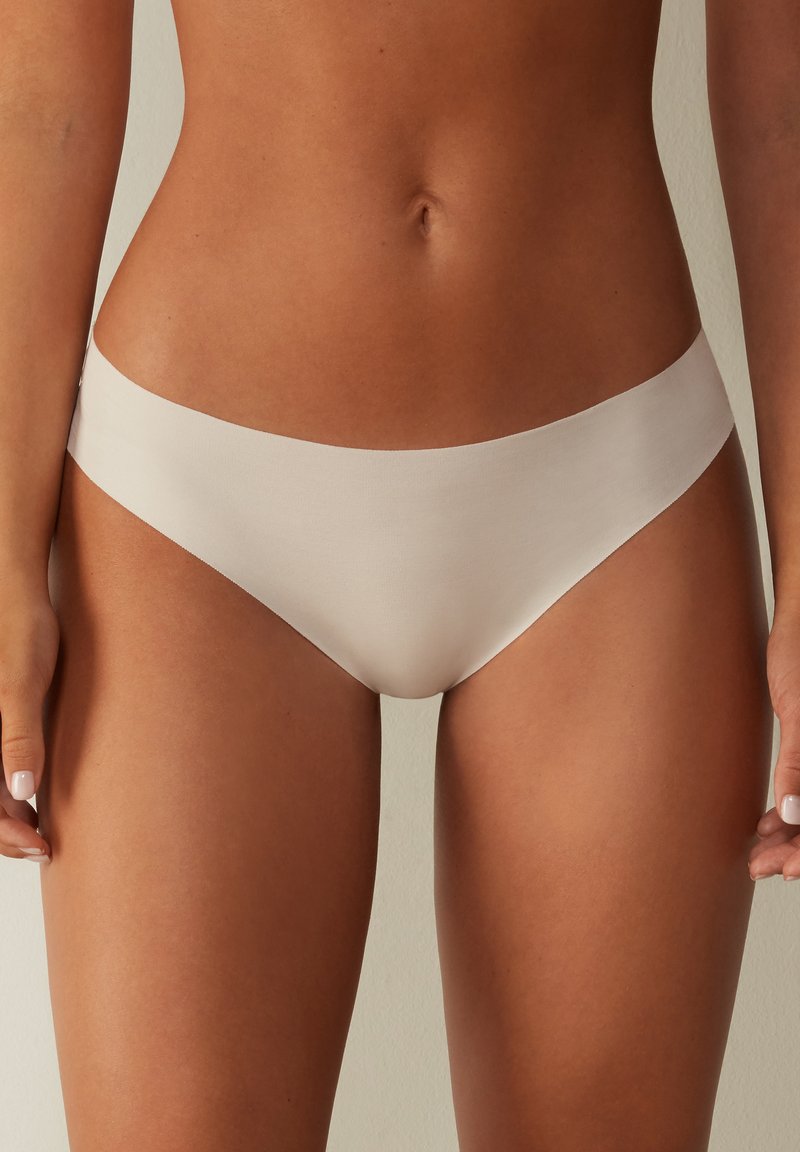Beige låg midja bikini-underkläder med slät, elastisk tyg och en sömlös design. Platt midjeband utan synlig sömnad eller hårdvara.