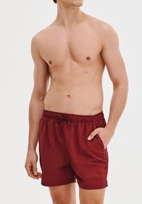 Czerwone szorty kąpielowe z elastycznym paskiem w talii i sznurkiem, z bocznymi kieszeniami. Materiał wydaje się lekki i gładki w dotyku.