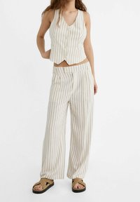 Pruhovaný, krémový a béžový, zkrácený top s výstřihem do V a předním zapínáním na knoflíky, spárovaný s širokými kalhotami ve stejném stylu a hnědými sandály.