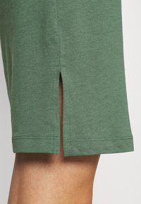 Zielona bawełniana koszulka z prostym krojem i bocznymi rozcięciami na dole. Posiada miękką teksturę i wzmacniane szwy.