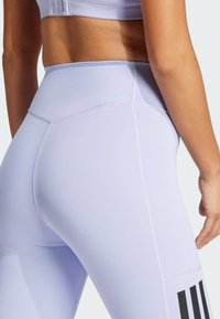 Liliowe legginsy z wysokim stanem, wykonane z miękkiego, elastycznego materiału, z czarnymi pionowymi paskami na dolnej części nogi oraz szwami płaskimi dla wygody.