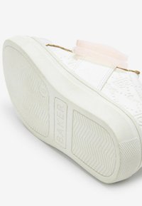 Basket blanche avec des détails texturés et une semelle en caoutchouc. Présente un accent en ruban rose et le mot "BAKER" embossé sur le côté.