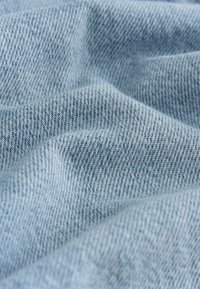 Világoskék farmeranyag látható halszálkamintával, puha tapintású és finom színárnyalat-változásokkal. Enyhén gyűrött, ami mélységet és lágy érzetet kölcsönöz neki.