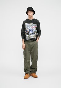 Black long-sleeve shirt with a colorful graphic print, olive green cargo pants, and brown boots. The hat is black and bucket-shaped.