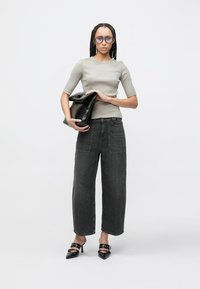 Top gris entallado, vaqueros negros de pierna ancha, bolso de mano negro y zapatos negros con tacón. Pelo alisado con trenzas y gafas grandes.