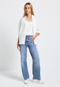 Bílá lněná košile na knoflíky přes bílý tílko, doplněná světlomodrými kalhotami s širokými nohavicemi. Celý outfit doplňují bílé tenisky.
