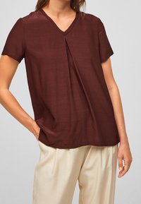 Blouse bourgogne à manches courtes et décolleté en V avec un détail plissé. Tissu doux, coupe décontractée et fentes sur les côtés pour un confort optimal.