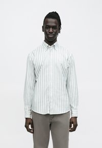 Raidallinen vaaleanvihreä ja valkoinen nappipaita, pitkähihaiset, kauluksellinen, valmistettu kevyestä kankaasta. Yhdistetty vaaleanharmaiden housujen kanssa.