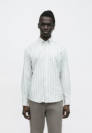 Gestreiftes Hemd mit Knöpfen, hellgrün und weiß, lange Ärmel, mit Kragen, aus leichtem Stoff. Getragen mit hellgrauer Hose.