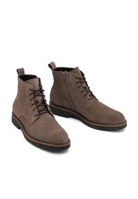 Botas de tobillo de ante marrón con diseño de cordones, cremallera lateral y suelas de goma. Presentan una textura suave y detalles de costura en contraste.