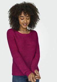 Pull en tricot magenta avec col rond, manches longues et bords côtes. Tissu texturé avec une coupe décontractée, associé à un jean en denim.