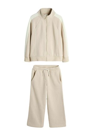Béžová fleecová súprava so zipovou bundou s kontrastnými panelmi na rukávoch a široké nohavice so sťahovacou šnúrkou a vreckami.