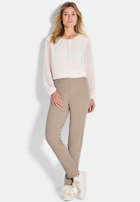 Lichte, lichtcrème blouse met plooi-details, gecombineerd met beige slim-fit broeken en witte sneakers. Zachte textuur en stijlvolle pasvorm.