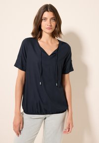 Top corto a maniche corte di colore blu navy con scollo a V e cordino regolabile. Realizzato in tessuto strutturato, ha una vestibilità rilassata e un orlo curvo.