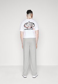 Vit croppad t-shirt med en svart och rosa grafik på baksidan, matchad med lösa gråa sweatpants och vita sneakers.