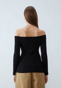 Czarny, odkryty top na ramionach z prążkowanego dzianiny z długimi rękawami, dopasowany krój, gładka faktura i delikatne rozszerzenie u dołu. Prosty i elegancki styl.