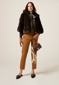 Brązowa kurtka z sztucznego futra, kwiecista bluzka, beżowe spodnie, brązowe skórzane rękawiczki, czarne płaskie buty oraz mała brązowa torebka z wzorzystą chustą.