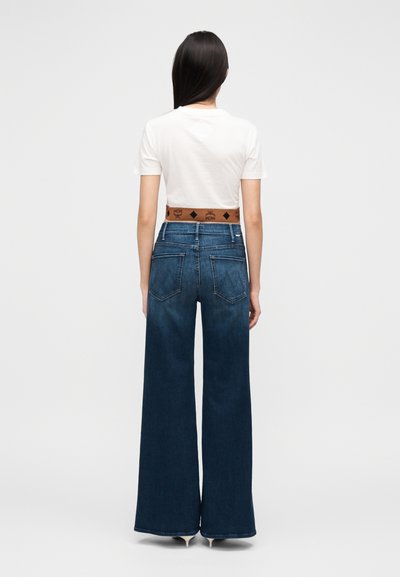 Τζιν παντελόνι φαρδύ στο πόδι, σε σκούρο μπλε χρώμα με ψηλή μέση. Φορεμένο με λευκό μπλουζάκι και καφέ ζώνη με λογότυπο. Λείο υλικό και κλασικός σχεδιασμός με πέντε τσέπες.