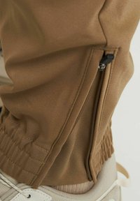 Tan gekleurde joggers van stof met elastische boorden, een ritssluiting aan de zijkant en een textuurpaneel bij de tailleband.