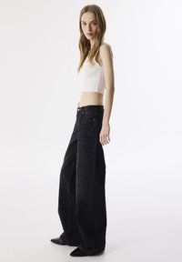Zwarte wijde jeans met textuur en een hoge taille, gecombineerd met een witte geribbelde cropped tanktop. Soepele, aansluitende uitstraling.
