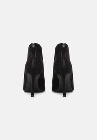 Botas de tobillo de ante negro con un diseño elegante, que cuentan con un tacón afilado, cremallera trasera y una textura suave.