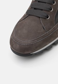 Zapatilla de ante gris con superficie texturizada, punta redonda y cordones grises. Cuenta con una suela de goma con un relieve prominente para mejor agarre.