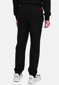 Zwarte joggerbroek met een elastische tailleband, slim fit en geribbelde manchetten, met een klein rood logo op de achterzak. Gecombineerd met witte sneakers.